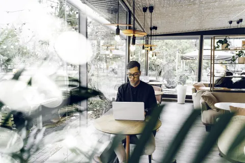 Smart looking young man sitting with a laptop in a cafe.